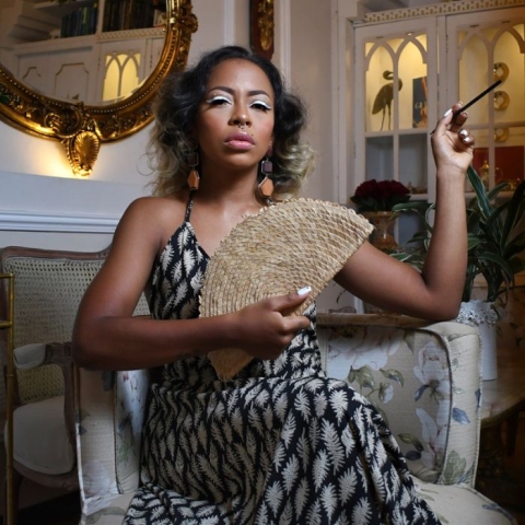 Fotografía de Keke Minowa sentada en una sala con vestido largo en la mano un abanico